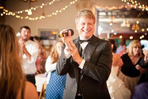 DJ Larry Hornyak in a black tuxedo clapping at a wedding.